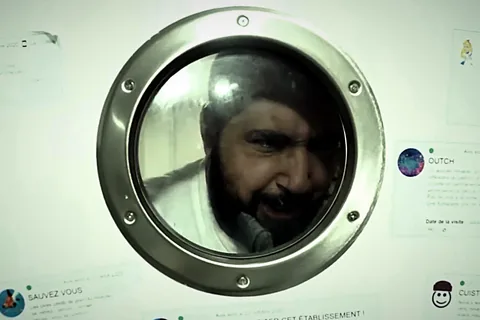 Le chef Magien derrière le hublot de sa cuisine, entouré d'avis une étoile