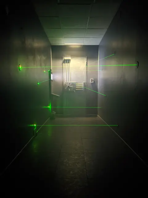 Couloir protégé par des lasers verts devant la porte blindée de la salle des coffres