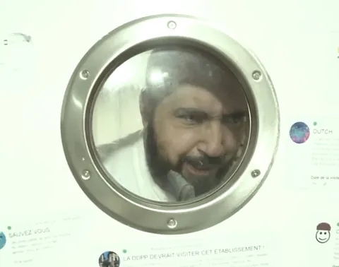 Chef Magien behind the porthole of his kitchen, surrounded by one-star reviews