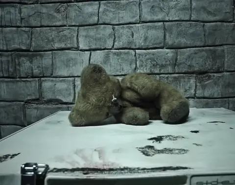 Vieux nounours posé sur un congélateur, dans le sous-sol du maniaque
