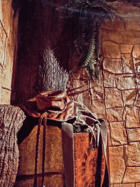Adventurer’s hat and whip on a crate, in front of a stone wall